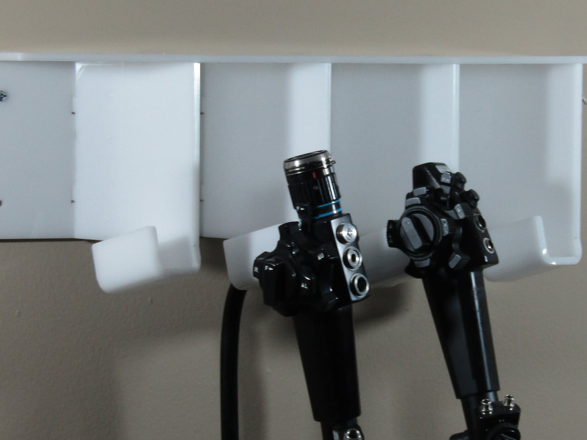 Two flexible video endoscopes hanging on a wall storage rack, set aside as-is