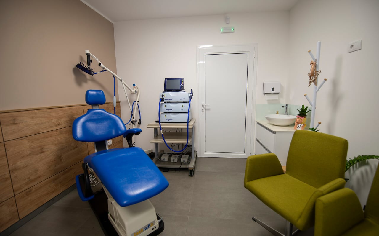 An empty clinical treatment room with a procedure chair and idle equipment on a cart as a practice winds down