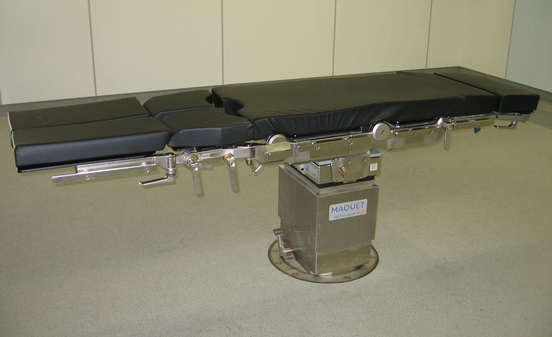 A MAQUET articulating procedure table with padded sections on a stainless-steel pedestal base