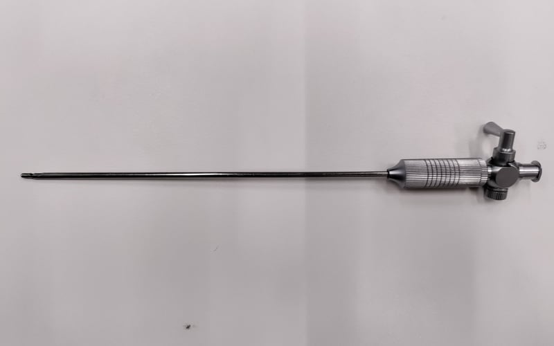 A used rigid rod-lens endoscope on an intake bench, showing the metal eyepiece, stopcock body with side port, and straight shaft