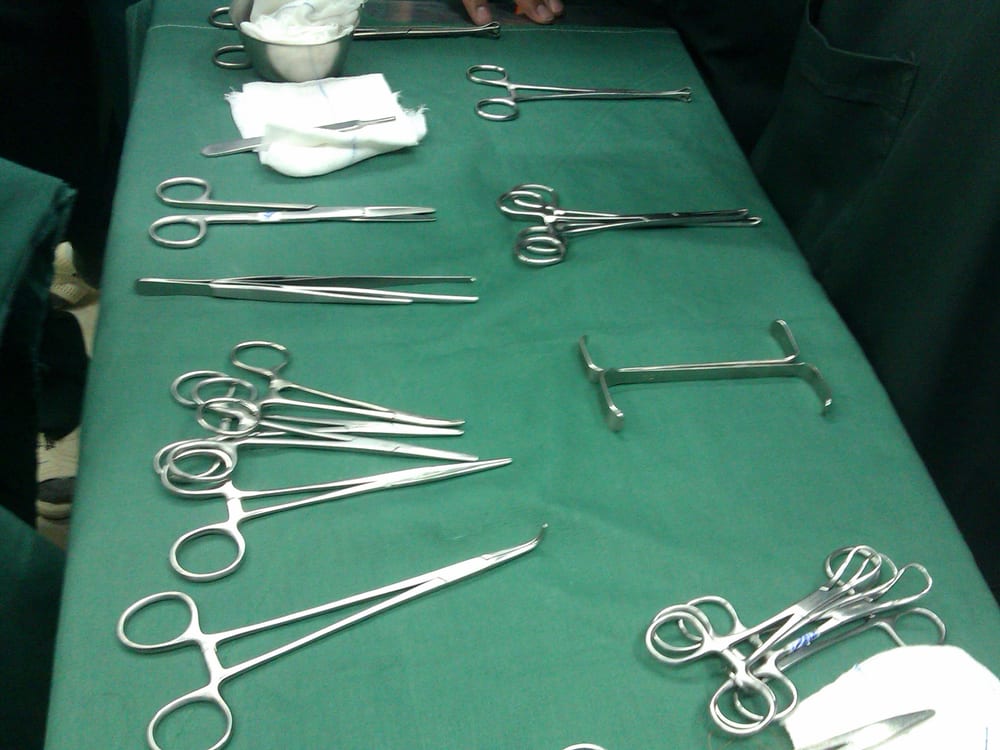 Used stainless surgical instruments — hemostats, forceps, scissors, and a retractor — laid out on a green drape, set aside as-is for pickup