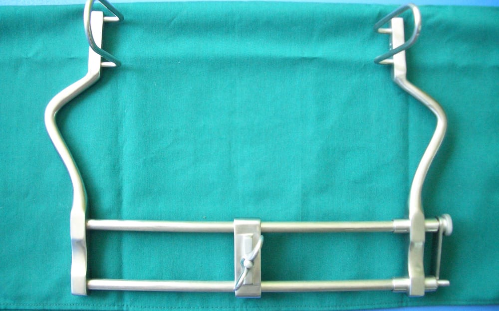 Self-retaining surgical retractor frame with deep lateral blades and a ratcheted spreader bar, used to hold open a deep spinal or back incision