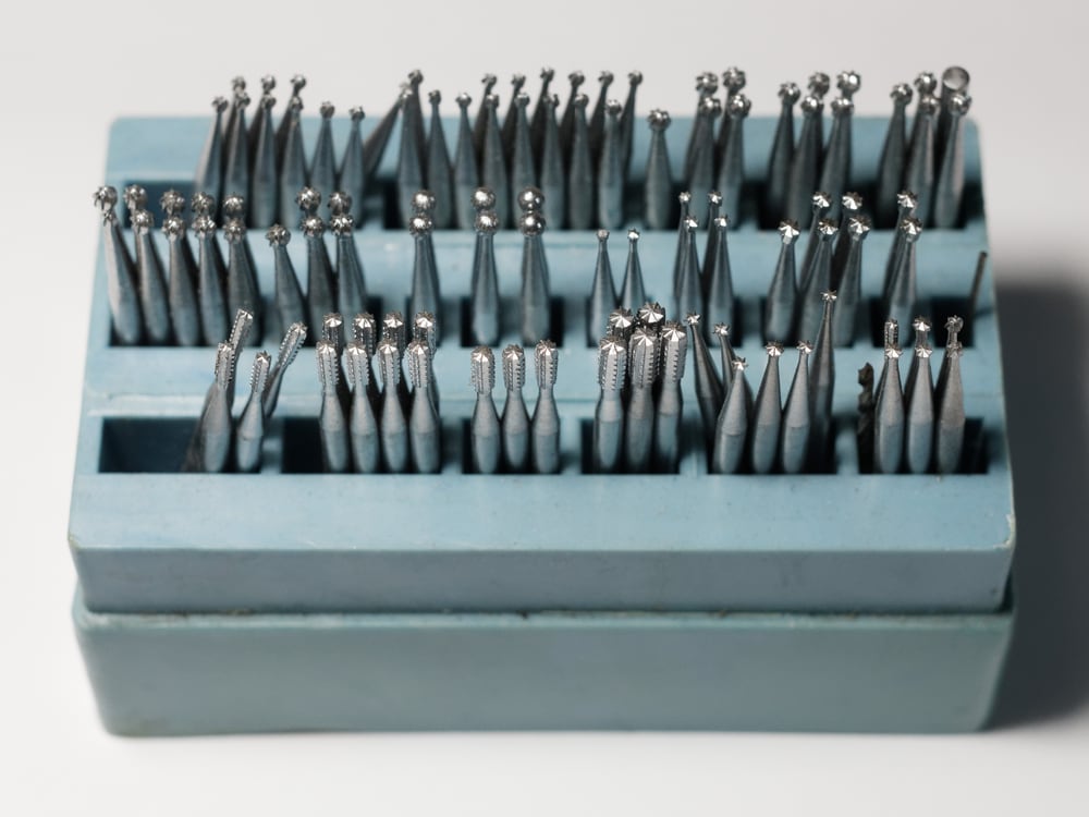 An assortment of surgical cutting burrs and drill attachments standing in a holder block