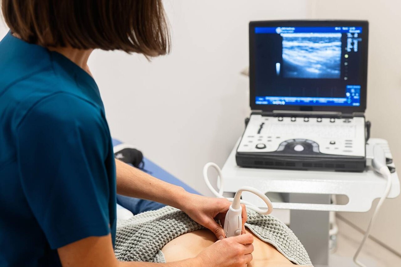 Clinician scanning a patient with an ultrasound probe beside the ultrasound system