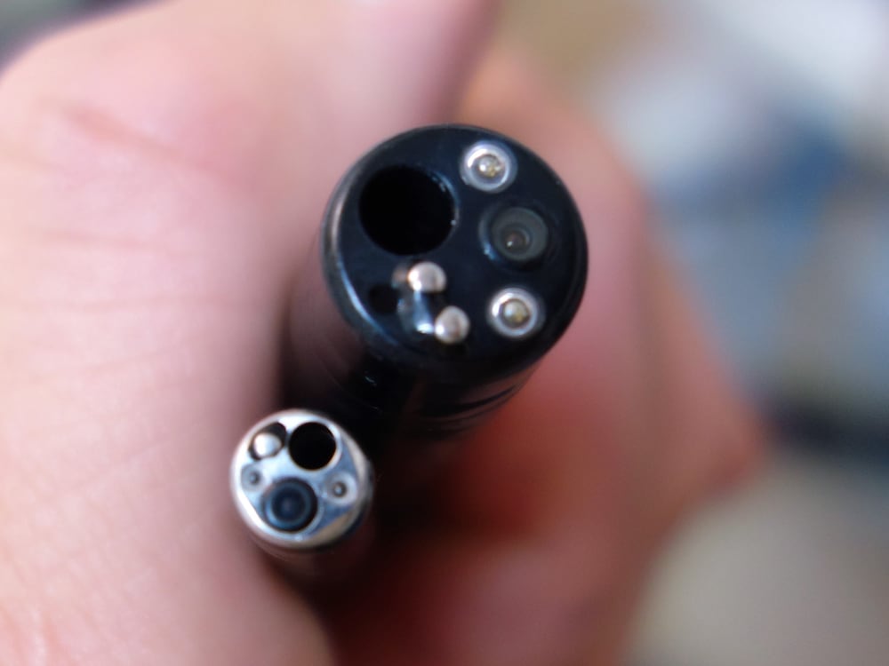Close-up of a used endoscopic camera scope's distal tip, showing the camera lens and fiber-optic light ports, held as-is