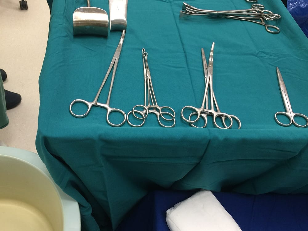 Used general-surgery hand instruments — clamps, forceps, scissors, and a retractor — laid out as-is on a surgical drape