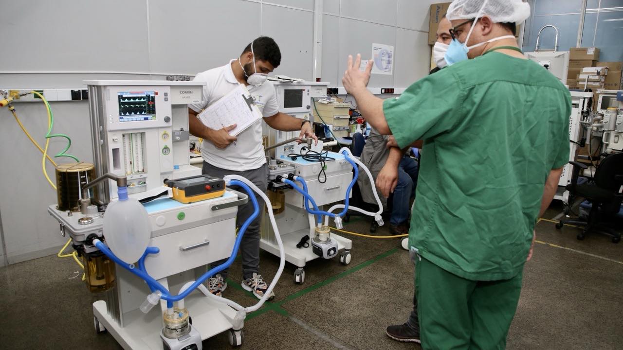 A technician reviewing equipment records on a clipboard beside anesthesia machines.
