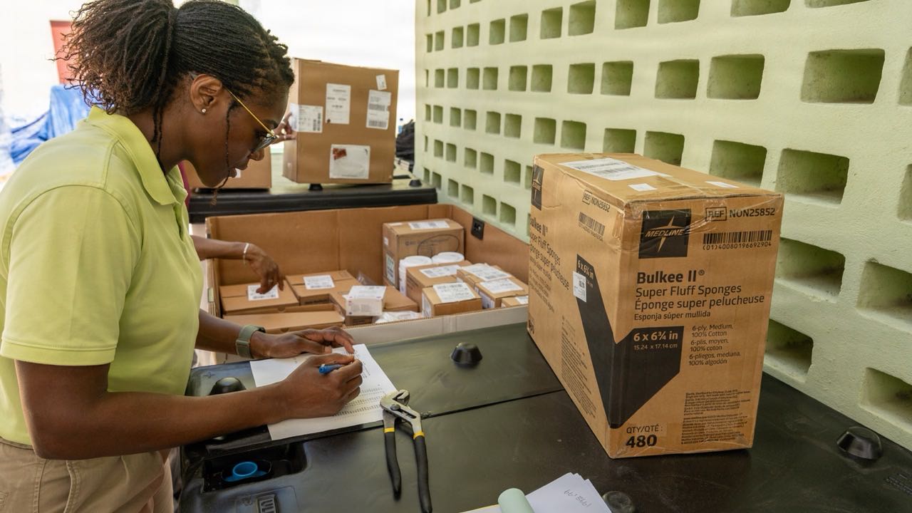 Staff member recording medical equipment details — model, reference number, and quantity — on an inventory sheet.