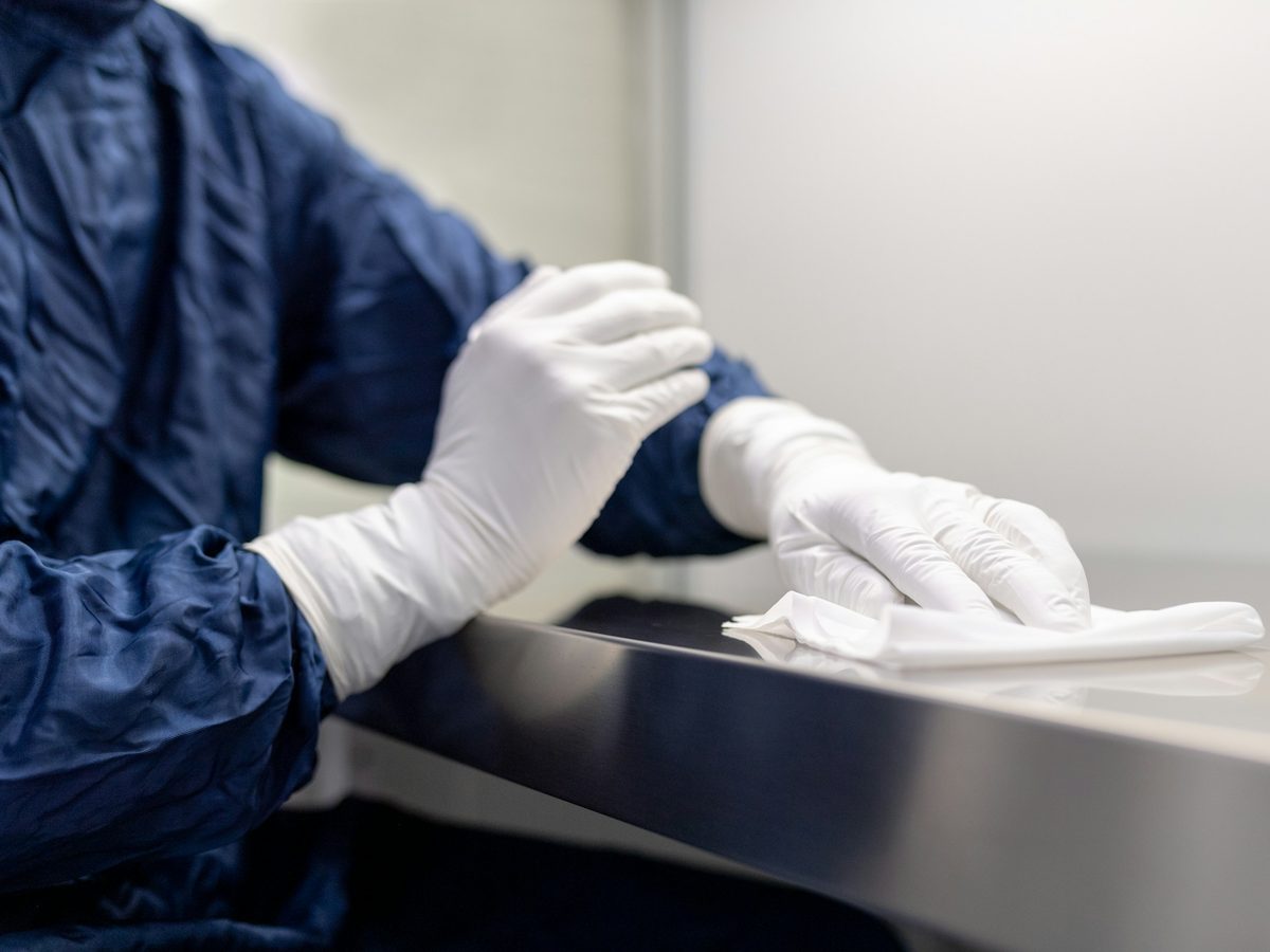 Gloved hands wiping down a stainless steel work surface