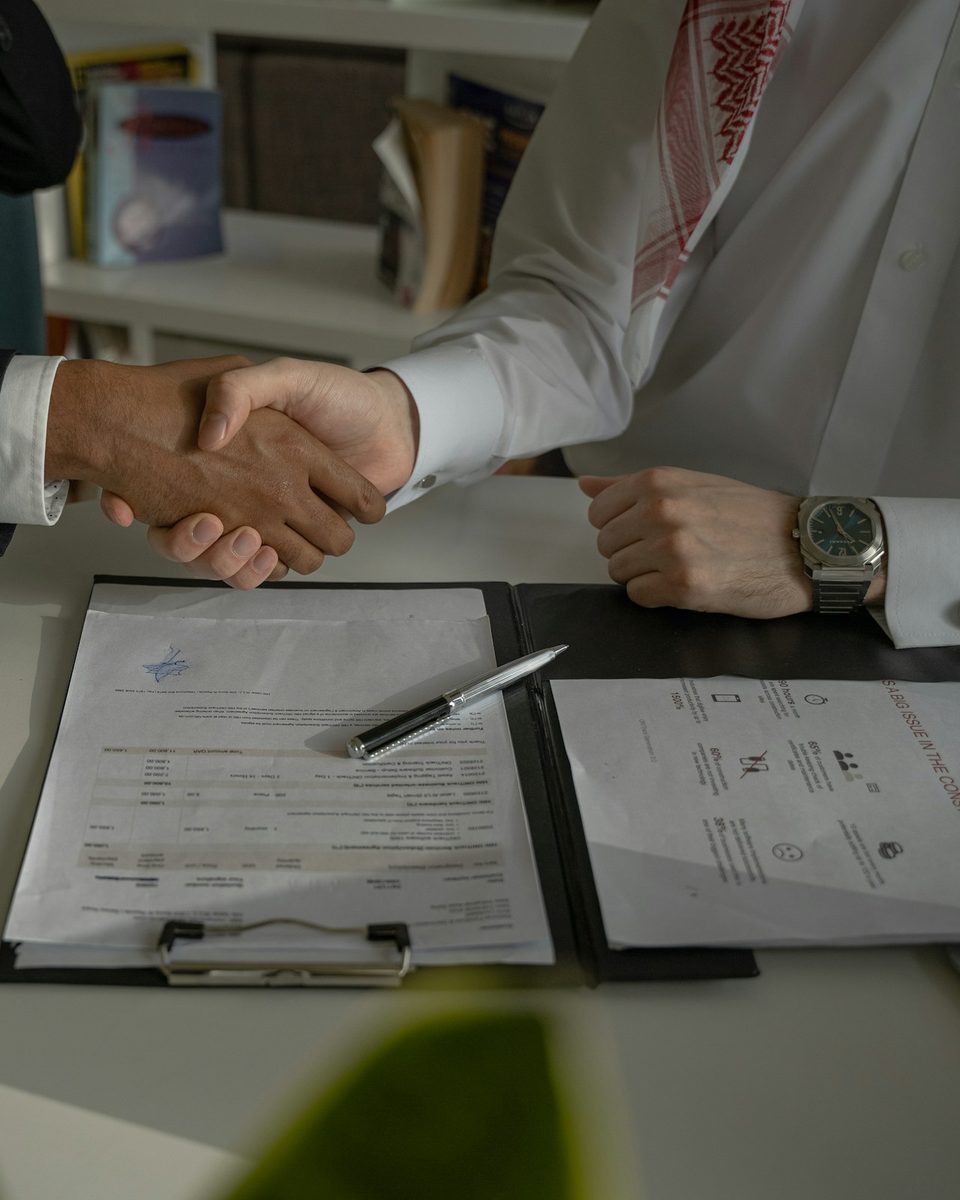 Two people shaking hands over a signed agreement on a clipboard